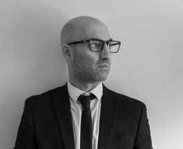 A man in a suit and tie standing in front of a wall